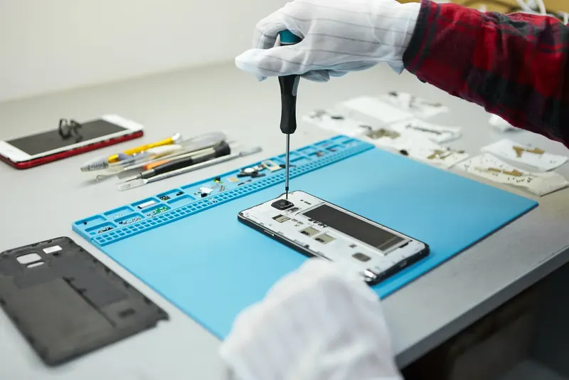 Tecnico con guanti che smonta uno smartphone su un tappetino antistatico